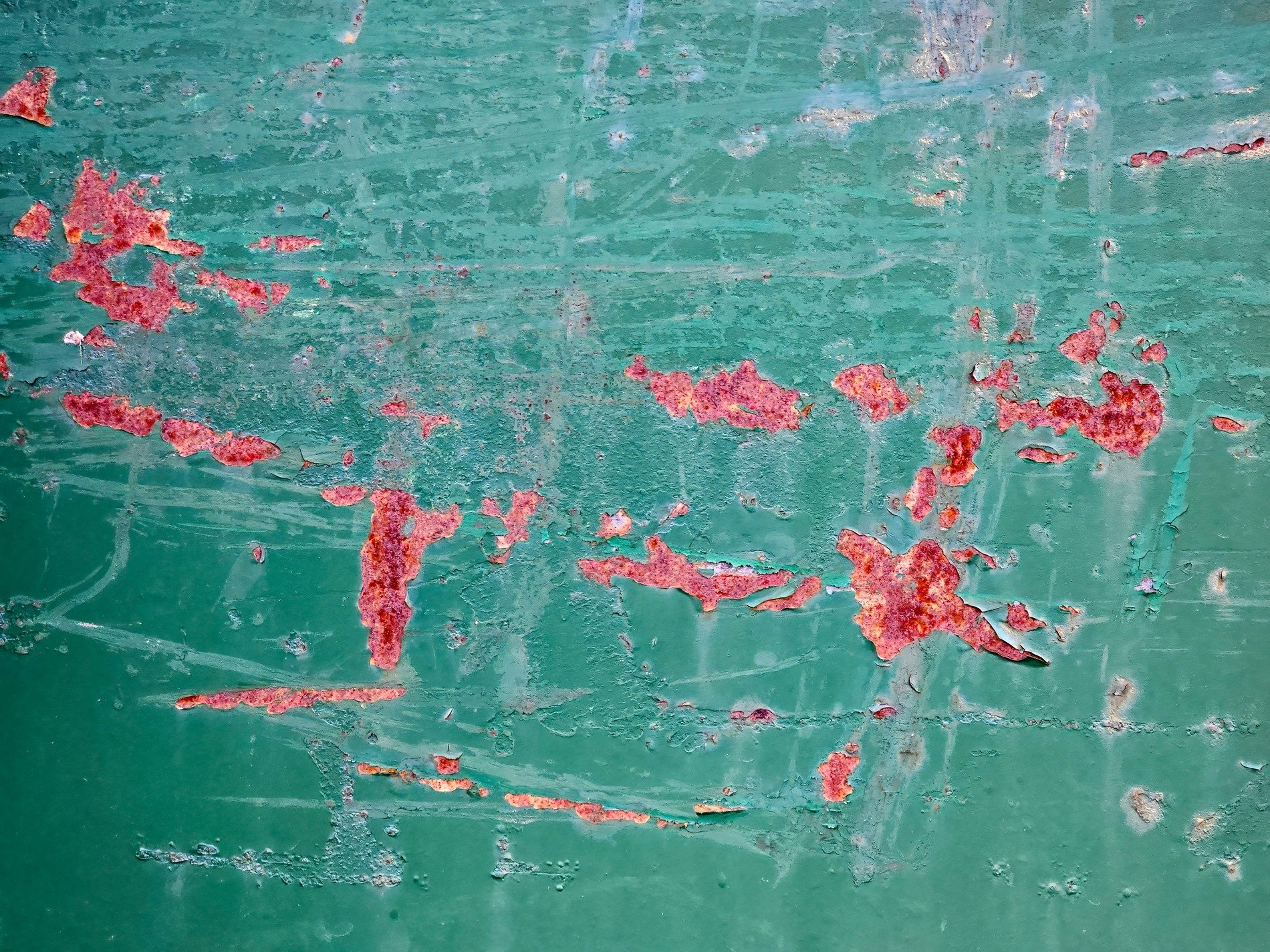 Teal paint curls away, iron oxide blooms in red, time etches the steel