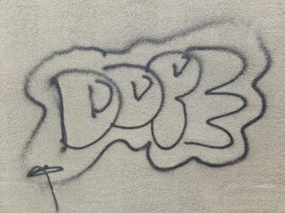 Black ink loops and curls, stone grain beneath spray paint lines, urban marks remain