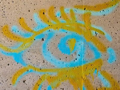 Blue and yellow paint, swirled upon the pitted wall, urban eye looks out