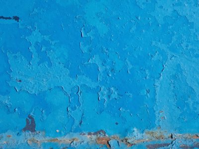 Blue layers chip away, weathered surface curls and falls, rusted edges show