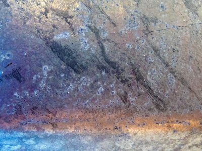 Blue metal scarred, heat blooms across the surface, time leaves spotted marks