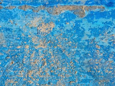 Blue paint chips away, rough concrete hides underneath, time wears down the wall