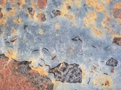 Blue paint flakes away, orange oxidation blooms, metal yields to time