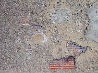Crumbled grey concrete, red brick reveals its texture, time peels back the skin
