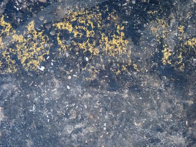Dark grit holds the dust, yellow paint scatters on ground, weathered stone remains