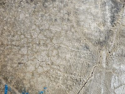 Fissures web the gray, weathered stone bears heavy weight, blue stains mark the edge