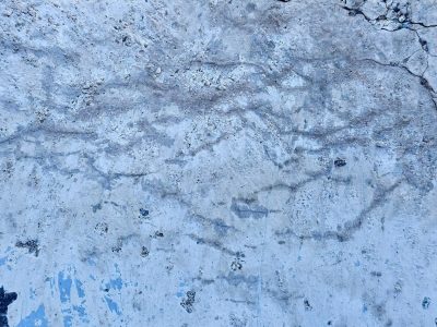 Frozen blue cement, rippled stains trace ancient lines, surface starts to break