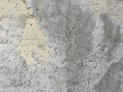 Gray wall wears its age, pitted surface tells a tale, layers fall away