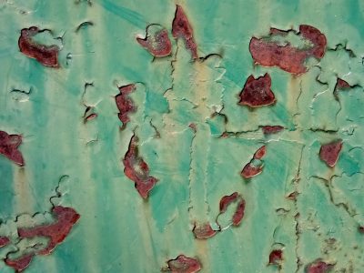 Green paint curls away, iron rust bleeds from within, metal skin decays