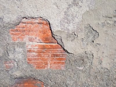 Grey stone falls away, red clay waits beneath the dust, time reveals the wall