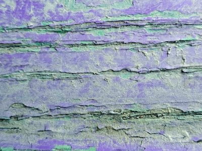 Purple layers flake, teal paint hides in the fissures, wood shows through the cracks