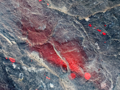 Red paint stains the rock, dark stone holds the heavy mark, texture tells the tale