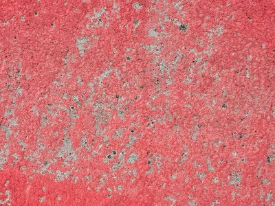 Red paint wears away, grey concrete breaks the surface, time erodes the hue