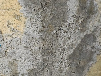 Rough gray wall stands worn, layers peel from gritty stone, time wears down the face