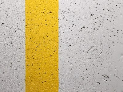 Rough wall of concrete, yellow stripe divides the grey, pitted paths remain