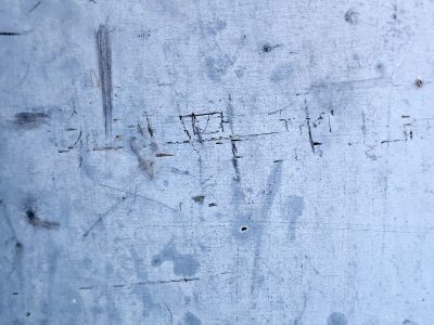 Scratched blue metal skin, dark marks dance across the field, time leaves its imprint