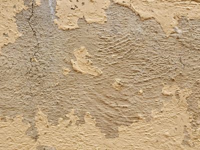 Tan paint flakes away, rough stone ridges hide beneath, time cracks the surface
