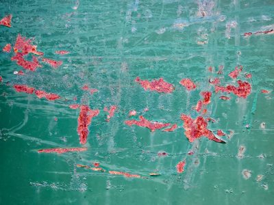 Teal paint curls away, iron oxide blooms in red, time etches the steel