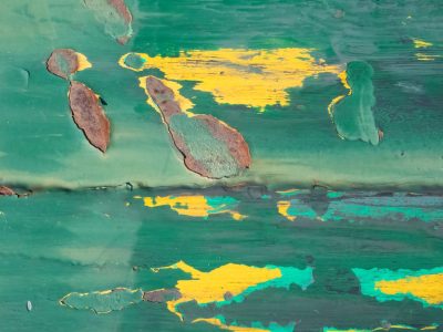 Teal paint flakes away, yellow streaks shine through the wear, rust marks time's decay