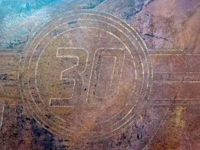 Thirty etched in dust, circles trace the worn metal, colors blur the line