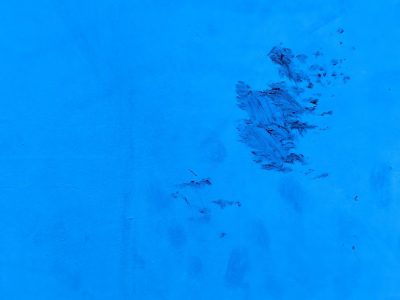 Vibrant blue field, dark marks scar the painted face, textures of the street