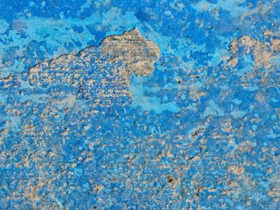 Vibrant blue flakes off, rough grey concrete hides beneath, time erodes the coat