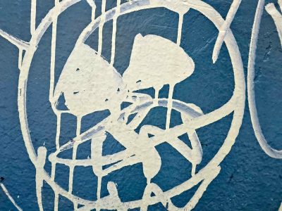 White paint drips on blue, rough wall holds the messy lines, urban shapes collide