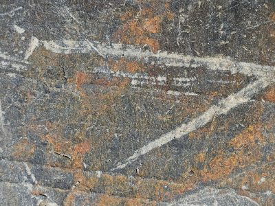 White veins cut through gray, rust stains the ancient surface, earth wears many marks