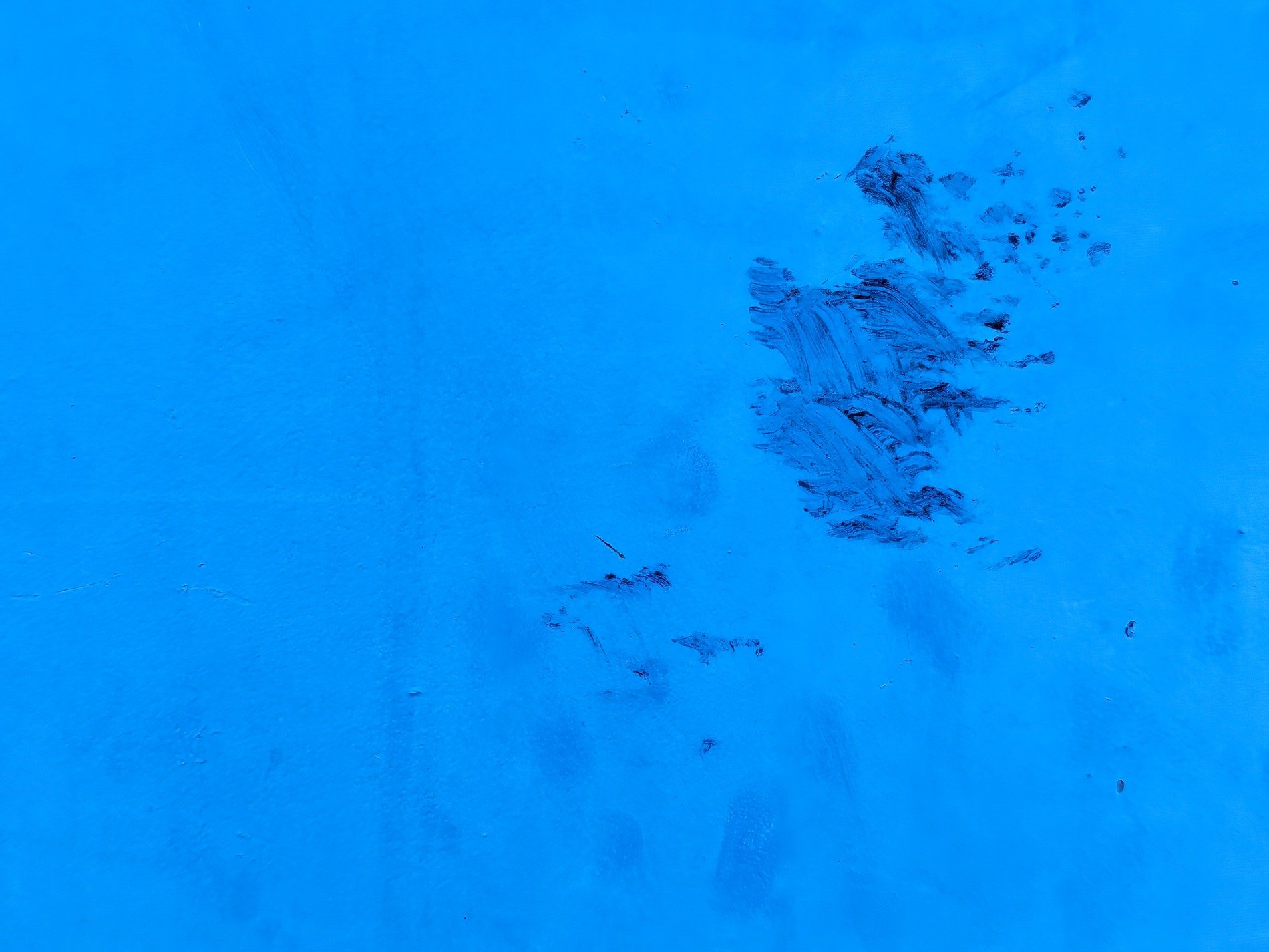 Vibrant blue field, dark marks scar the painted face, textures of the street