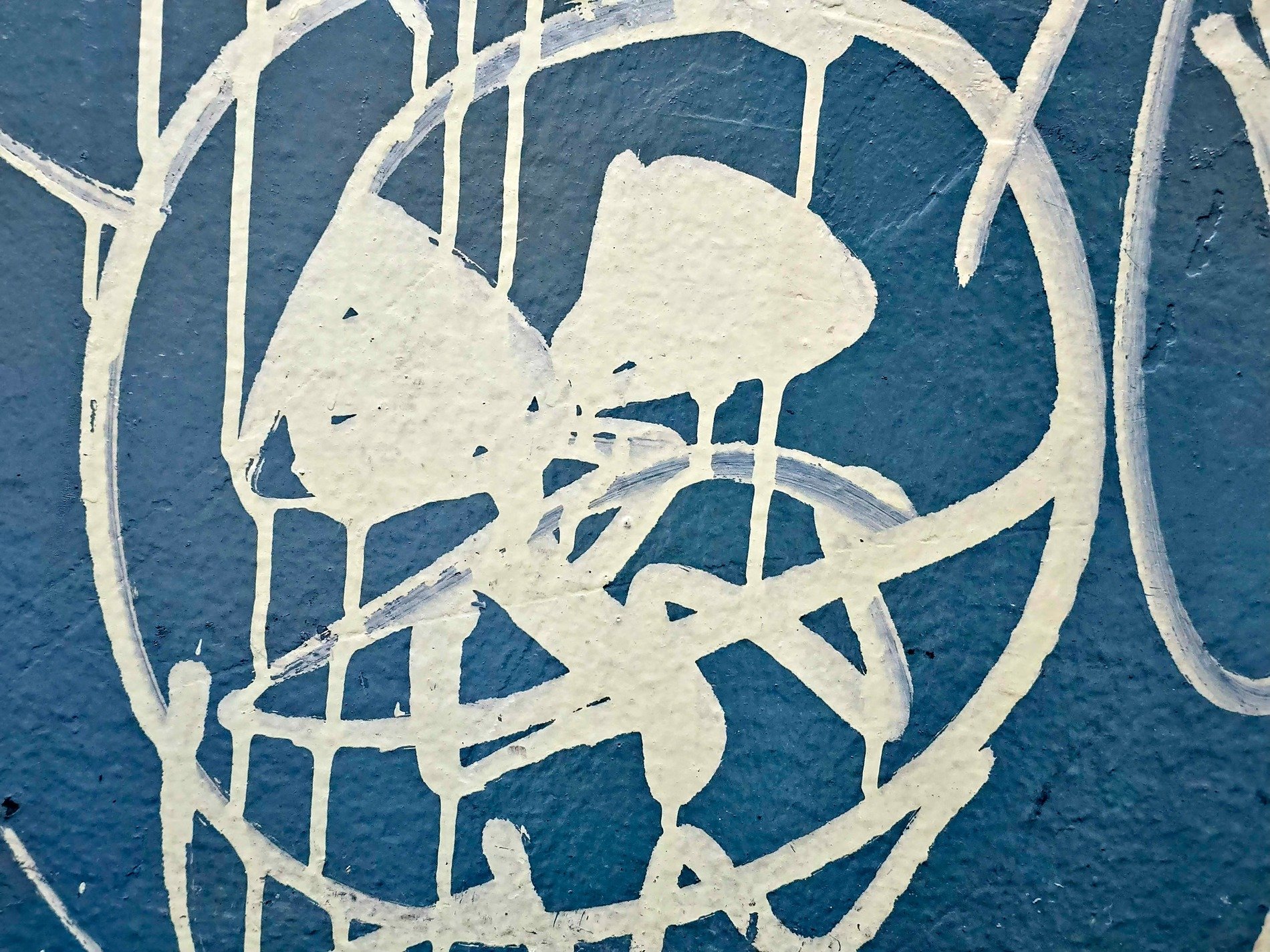 White paint drips on blue, rough wall holds the messy lines, urban shapes collide